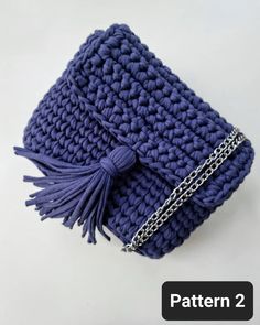 a crocheted blue purse with chain and tassels on the front, sitting on a white surface