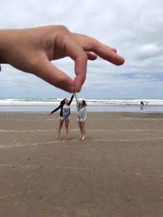 two people standing on the beach with their hands in the air and one person reaching for something