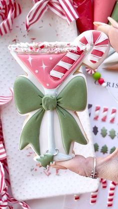 a hand holding a decorated cookie in the shape of a martini with green bow and candy canes