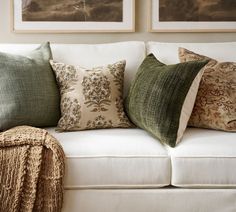 a white couch with green and brown pillows on it's back cushions are next to a throw blanket