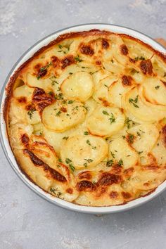 a dish with potatoes and parsley in it on a gray table top next to a wooden utensil