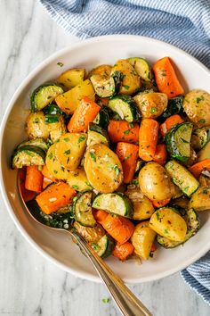 a white bowl filled with roasted vegetables on top of a marble counter next to a fork