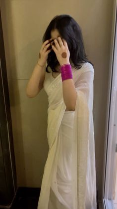 a woman in a white sari holding her hands up to her face while standing next to a door