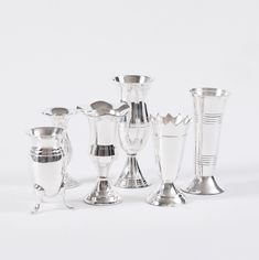 a group of silver vases sitting next to each other on top of a white surface