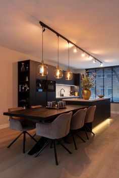 a dining room table with chairs and lights hanging from it's ceiling over the kitchen island