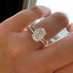 a woman's hand with a diamond ring on top of her finger, next to a window