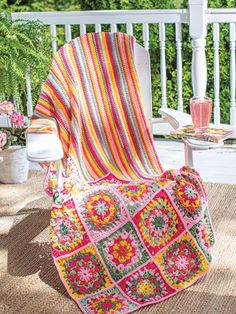 a colorful blanket sitting on top of a white chair next to a potted plant