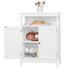 a white cabinet with two doors and some books on it's shelf next to a flower vase