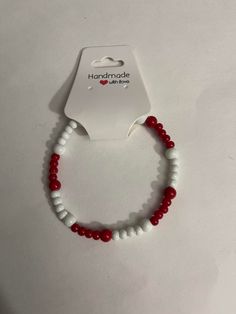 A bracelet with red and white beads fastened on a clear elastic cord (one size fits most) Cheap Red Beaded Bracelets With Letter Beads, Cheap Red Beaded Bracelets, Red And White Beaded Bracelet, White Stretch Bracelet With Colorful Beads, Trendy White Beaded Bracelets, Casual White Hand-strung Wristband, Red Trendy Stretch Bracelet With Letter Beads, White Beaded Stretch Bracelet As Gift, Trendy Red Stretch Bracelet With Letter Beads