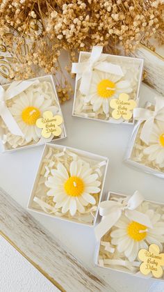 four small white boxes with yellow and white flowers in them sitting on a table next to dried grass