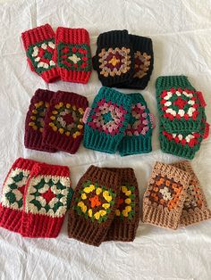 nine crocheted mittens laid out on a white sheet, all in different colors