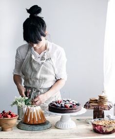 a woman cutting into a cake on top of a wooden table next to other desserts