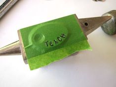 a green piece of paper with the word teach written on it is being held by a pair of scissors