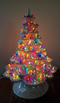 a brightly colored christmas tree is lit up on a white plate with colorful beads and bows