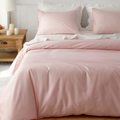 a bed with pink sheets and pillows on top of it next to a night stand