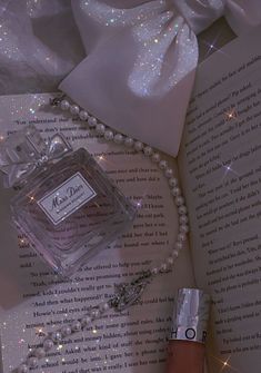 a bottle of perfume sitting on top of an open book next to pearls and a necklace