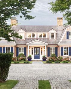 a large house with blue shutters and brick walkway leading to the front door area