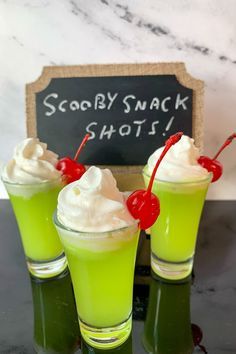 three glasses filled with green liquid and topped with whipped cream next to a chalk board