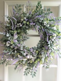 a wreath hanging on the front door with purple flowers and greenery around it's edges