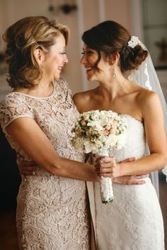 two women standing next to each other in front of a mirror holding bouquets and smiling