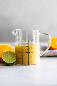 a measuring cup filled with orange juice next to sliced lemons and lime wedges