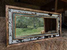 a mirror sitting on top of hay in front of a barn door with trees and grass behind it