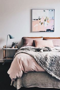 a bed with pink sheets and blankets in a bedroom next to a painting on the wall