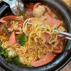 a bowl filled with noodles, meat and veggies next to a silver spoon