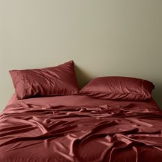 an unmade bed with red sheets and pillows