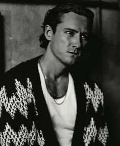 a man in a sweater is leaning against a wall and looking off to the side