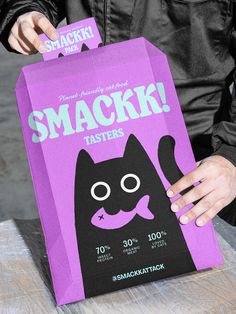 a person holding up a purple bag with a black cat on it's face