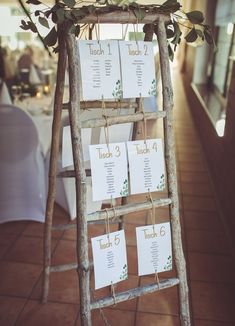 a wooden ladder with seating cards attached to the side and greenery growing on top