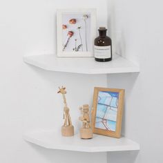 two white shelves with pictures and other items on them in a corner next to a framed giraffe