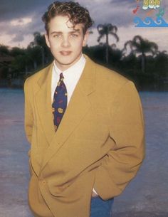 a young man in a suit and tie standing by the water with his hands on his hips