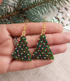 someone is holding their christmas tree beaded earrings in the palm of their hand,