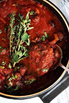 a pot filled with meat covered in sauce and garnished with herbs