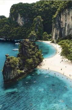 people are swimming in the clear blue water next to an island that is surrounded by cliffs