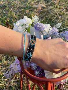 a woman's arm with two bracelets on it and flowers in the background