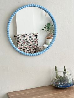 a round mirror hanging on the wall above a table with a vase and cactus in it