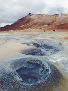 some people are walking in the distance on a barren area with blue water and brown hills