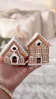 two small houses made out of gingerbread are held in front of a white bed