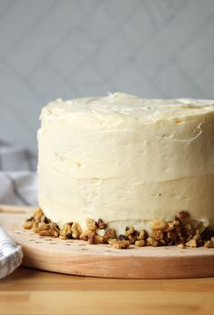 a cake with white frosting and walnuts on a wooden board next to a napkin