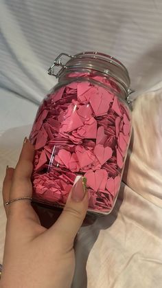 a person holding a jar filled with pink paper hearts