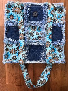 a blue and brown flowered bag on top of a wooden floor with a button in the middle