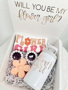 a white box with flowers, sunglasses and a flower girl bottle in it that says will you be my flower girl?