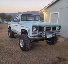 a white truck parked in front of a house on top of a dirt field next to a building