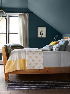 a bed sitting under a window in a bedroom next to a wooden table and chair