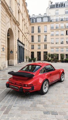 a red sports car parked in front of a large building on a cobblestone street