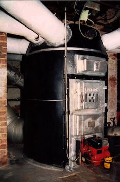 a large black refrigerator sitting inside of a room next to pipes and piping equipment