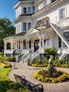 a large white house with lots of flowers in the front yard and stairs leading up to it